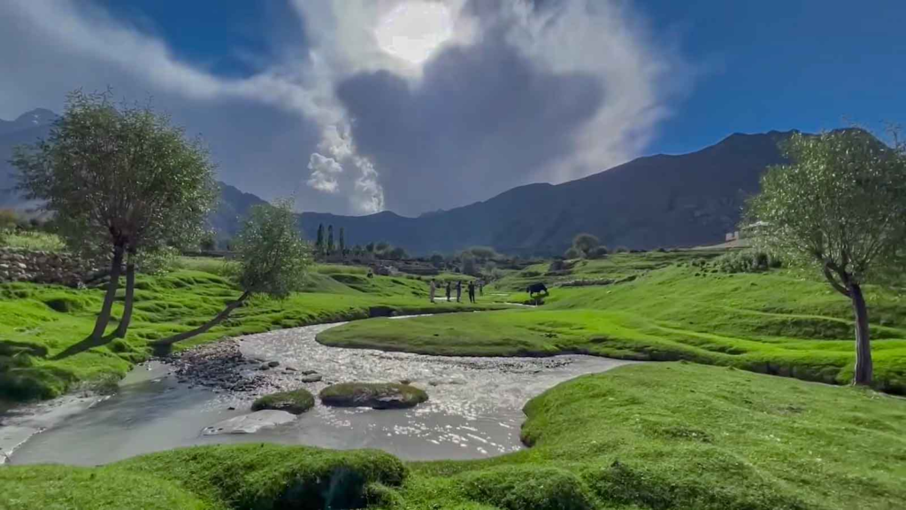 Stream winding through green meadows in Bilamik Valley, Rondu, beneath mountain ridges and clouds