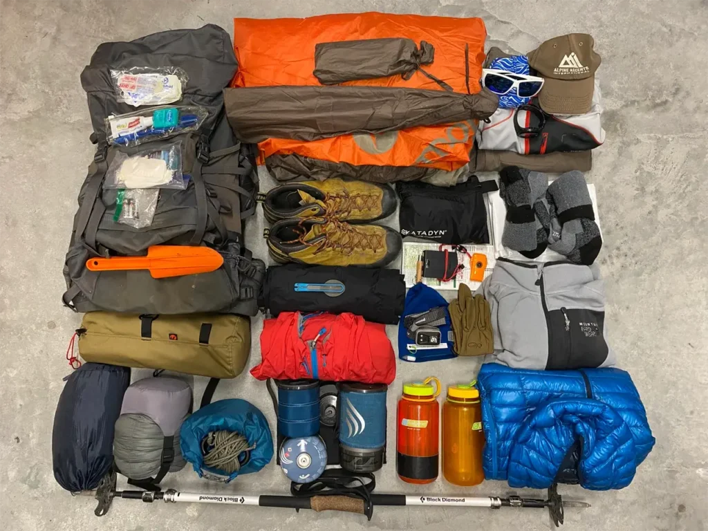 Lightweight backpacking checklist gear laid out on a floor: pack, tent, sleeping bag and stove