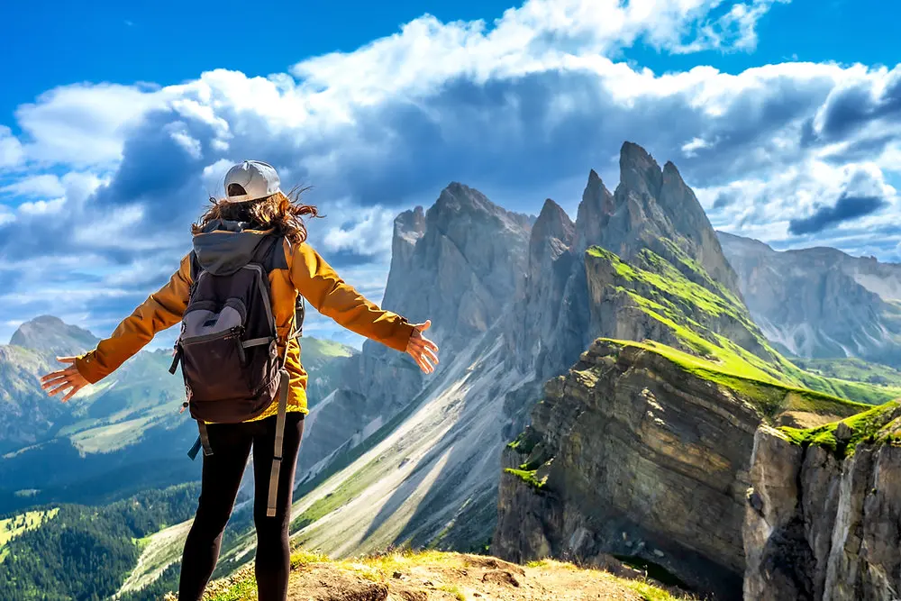 Climber in a red jacket walking a narrow snow ridge above a sea of cloud, mountain summit feeling.